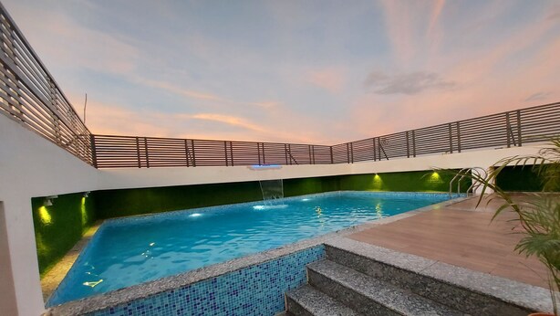 A swimming pool with a tiled edge, a set of stairs leading down to the water, and a railing above.