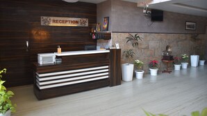 A reception desk with a sign reading "RECEPTION," a flat-screen TV mounted on the wall, and several potted plants arranged in a row.