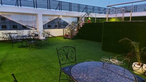 A rooftop terrace with artificial grass, metal furniture, and a glass table.