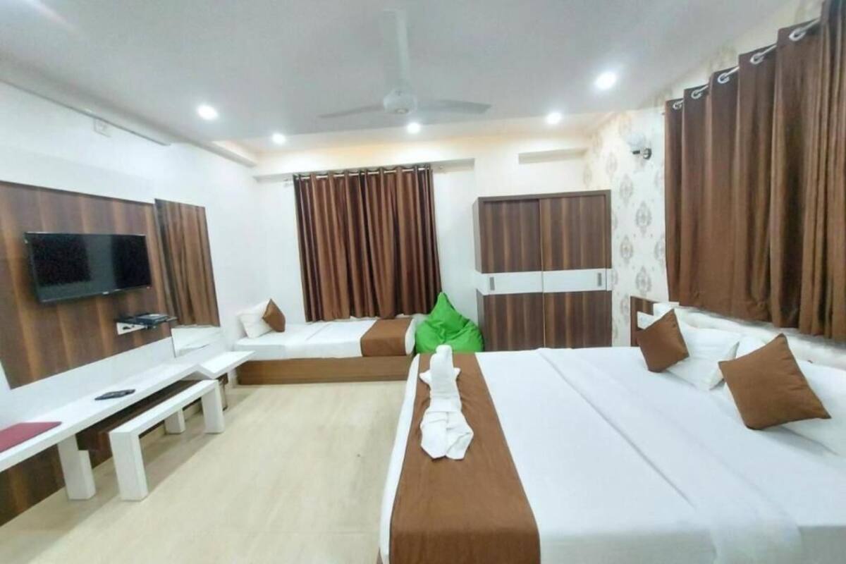 Une chambre d’hôtel avec deux lits, une télévision, un banc et des rideaux.
