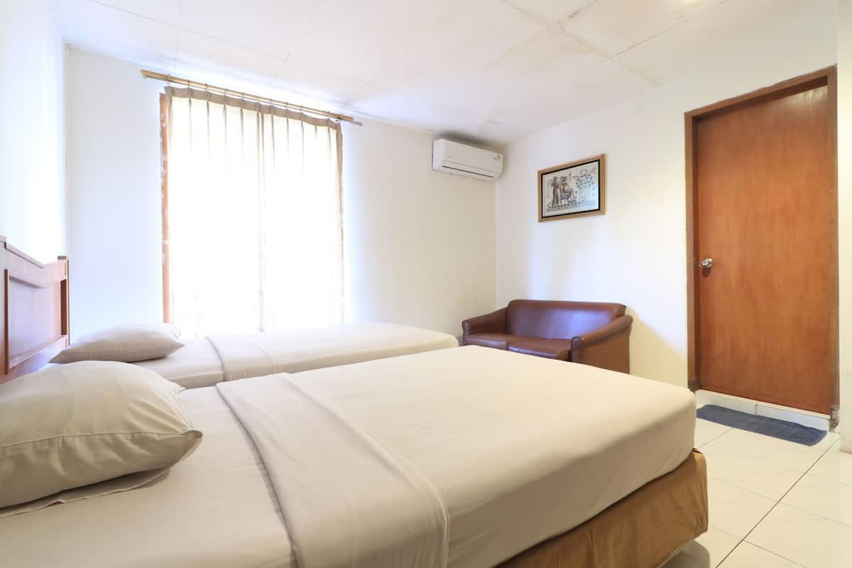 Une chambre d’hôtel avec deux lits, une porte en bois, un appareil de climatisation et une fenêtre avec des rideaux.
