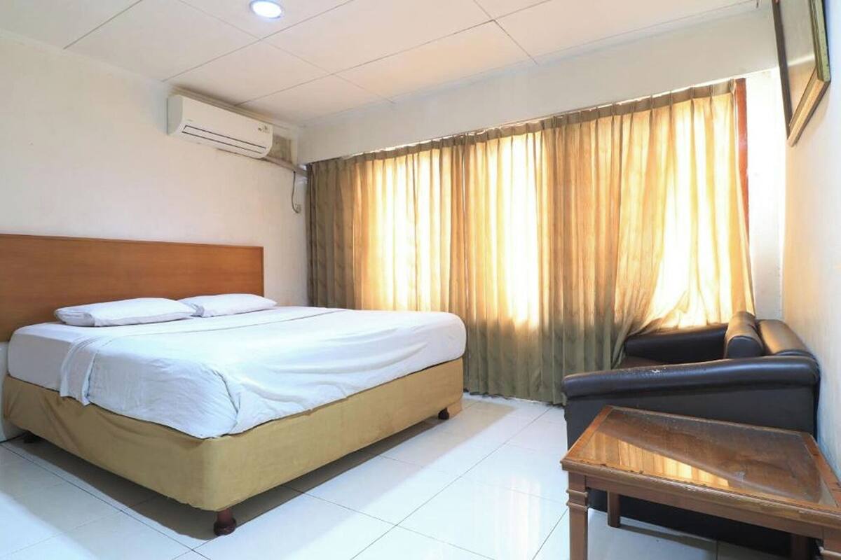 Une chambre d’hôtel avec un lit, une petite table, une chaise et une fenêtre avec des rideaux.