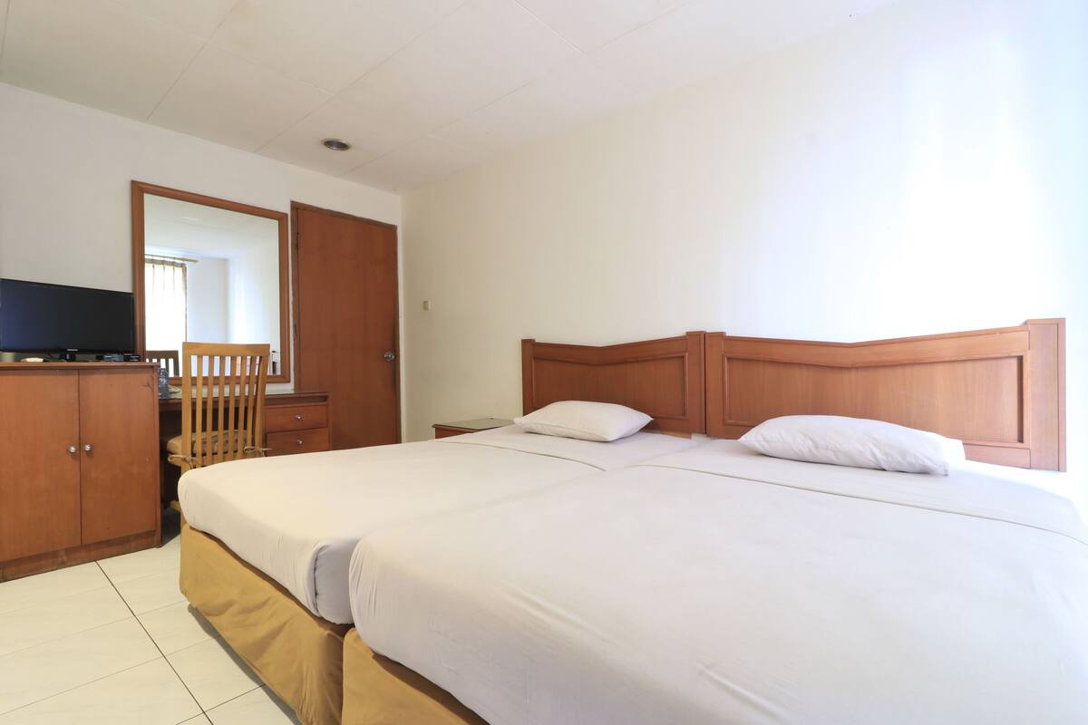 Une chambre d’hôtel avec un grand lit, une tête de lit en bois, un téléviseur posé sur une commode en bois et un miroir au mur.