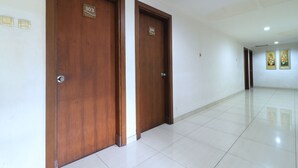 Un couloir avec deux portes en bois, portant les numéros 303 et 304, qui donnent accès à des pièces. Le sol est carrelé et les murs sont blancs.