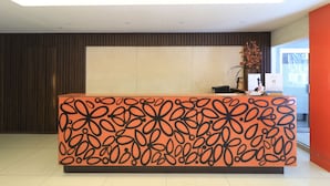 Un comptoir d’accueil au design original, un mur revêtu de panneaux en bois foncé et une fenêtre avec des stores.