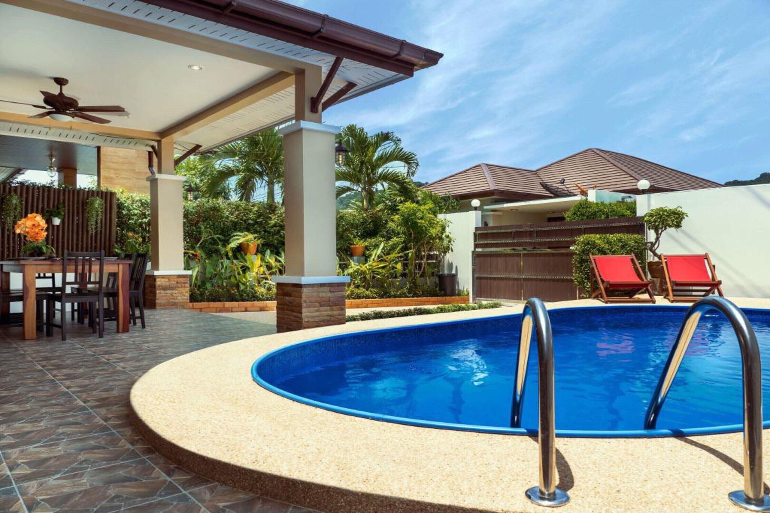 Una piscina con un porche techado, una mesa de comedor y sillas reclinables rojas.