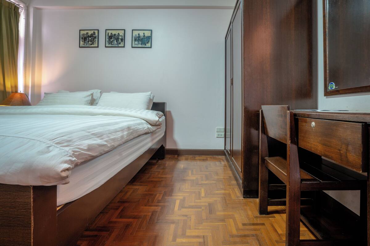 A bedroom with a bed, wooden floor, and a desk.