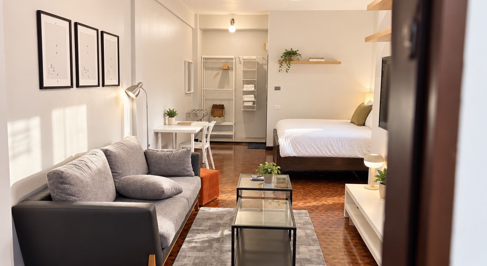 Una sala moderna con un sofá, una mesa de centro y una cama. Hay un comedor con una mesa y sillas, y una pequeña cocina con un refrigerador y una planta.