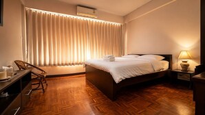 A hotel room with a bed, a desk, a chair, a nightstand, and a lamp. - Sabai house (Chiang Mai)