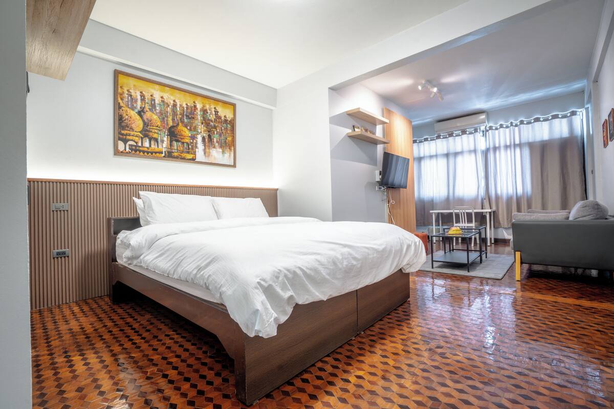 A hotel room with a large bed, a painting on the wall, a TV, and a sofa.