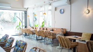 A restaurant with wicker chairs and tables, a large window with curtains, and a wall-mounted fan. - Sabai house (Chiang Mai)