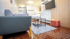 A modern living room with a grey sofa, a small table, a pink ottoman, and a TV mounted on the wall. - Sabai house (Chiang Mai)