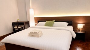 A hotel room with a large bed, a bedside table, a nightstand, and a wall-mounted lamp. - Sabai house (Chiang Mai)