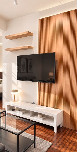 A modern living room with a flat-screen TV mounted on a wall, a white entertainment unit below, and a patterned floor. - Sabai house (Chiang Mai)
