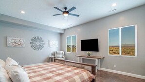 A bedroom with a bed, a ceiling fan, a TV, and a window with a desert view. - Charlotte: Large Groups + Private Hot Tub + Roof Top Deck (Hurricane)