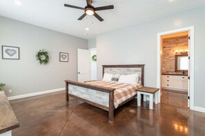 A bedroom with a wooden bed, a ceiling fan, and a view into the kitchen. - Charlotte: Large Groups + Private Hot Tub + Roof Top Deck (Hurricane)