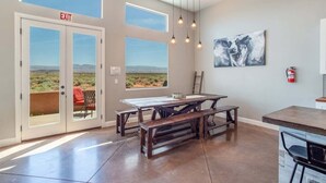 A spacious room with a large table and benches, a painting on the wall, and an exit door with a view of the outdoors. - Charlotte: Large Groups + Private Hot Tub + Roof Top Deck (Hurricane)