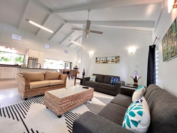 Een ruime woonkamer met een hoge plafond en een plafondventilator, en een groot raam dat voor natuurlijk licht zorgt.