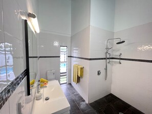 Een badkamer met witte betegelde wanden, een douchegedeelte met zwart-wit tegels, een witte wastafel met spiegel en een gele handdoek aan de muur.