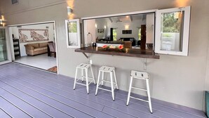 Un espace cuisine extérieur moderne, doté d’un comptoir-bar, de trois tabourets blancs et d’un grand miroir.
