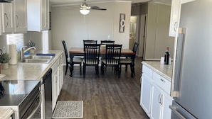 Una cocina moderna con armarios blancos, un comedor con mesa y sillas de madera, y un ventilador de techo.