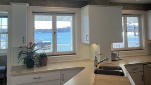 Ett kök med vita skåp, en dubbeldiskho och utsikt över en sjö.