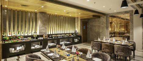 A modern dining area with multiple tables set for service, a buffet with various food items, and a stylish interior design.