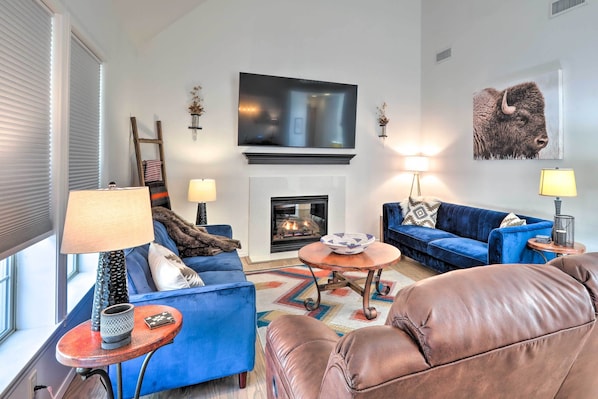 Un salon doté d’une cheminée, de canapés bleus, d’un fauteuil en cuir marron et d’un téléviseur à écran plat fixé au-dessus de la cheminée.