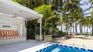 A pool area with a white deck, striped cushions, and a sign indicating a beach direction.