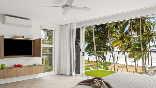 A bedroom with a bed, a TV mounted on the wall, and a view of the beach.