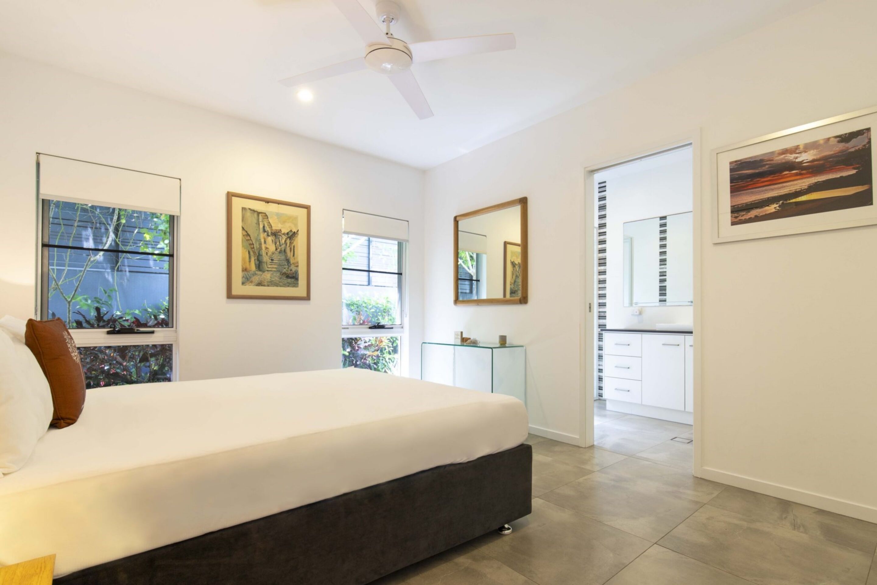 Une chambre moderne avec un grand lit, un ventilateur de plafond et une vue sur la cuisine par une porte ouverte.