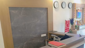 A reception desk with a marble backdrop, a clock, and a small plant. - Hotel Fun Park Sanand (Sanand)