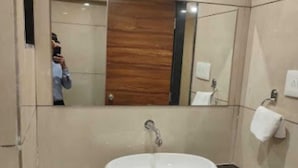 A bathroom with a white sink, a mirror, and a towel dispenser. - Hotel Fun Park Sanand (Sanand)