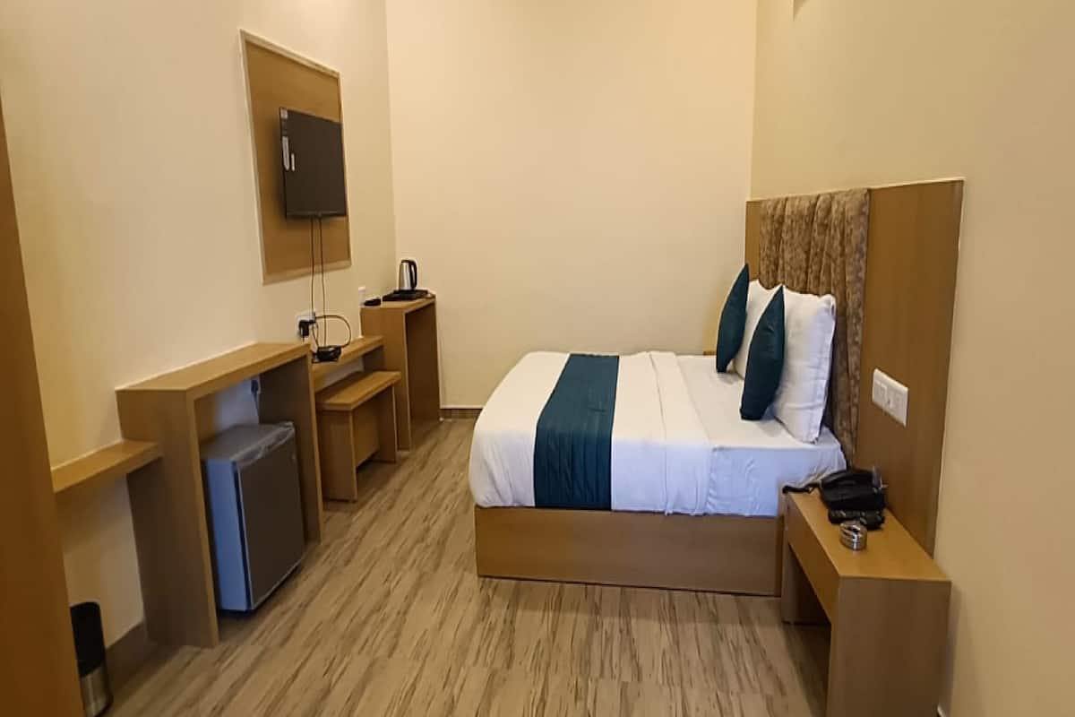 A compact hotel room with a single bed, a desk, a chair, a small TV, and a coffee maker.