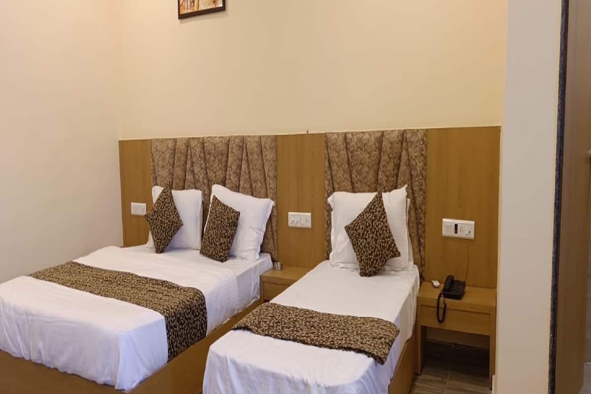 A hotel room with two single beds, each with a patterned bedspread and matching pillows. There is a bedside table with a phone and a power outlet.