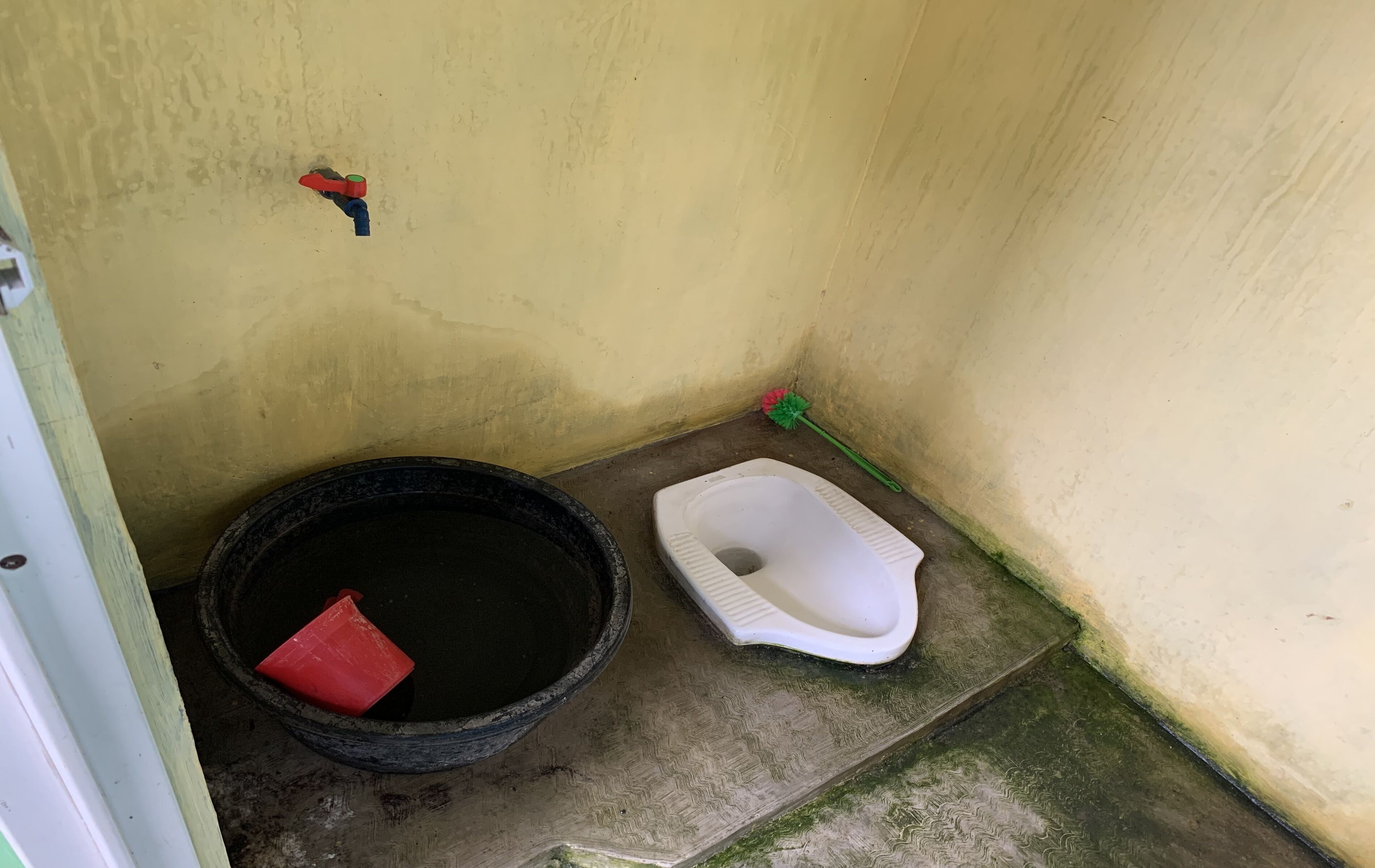 Un petit espace clos comprenant des toilettes, un seau et un balai.