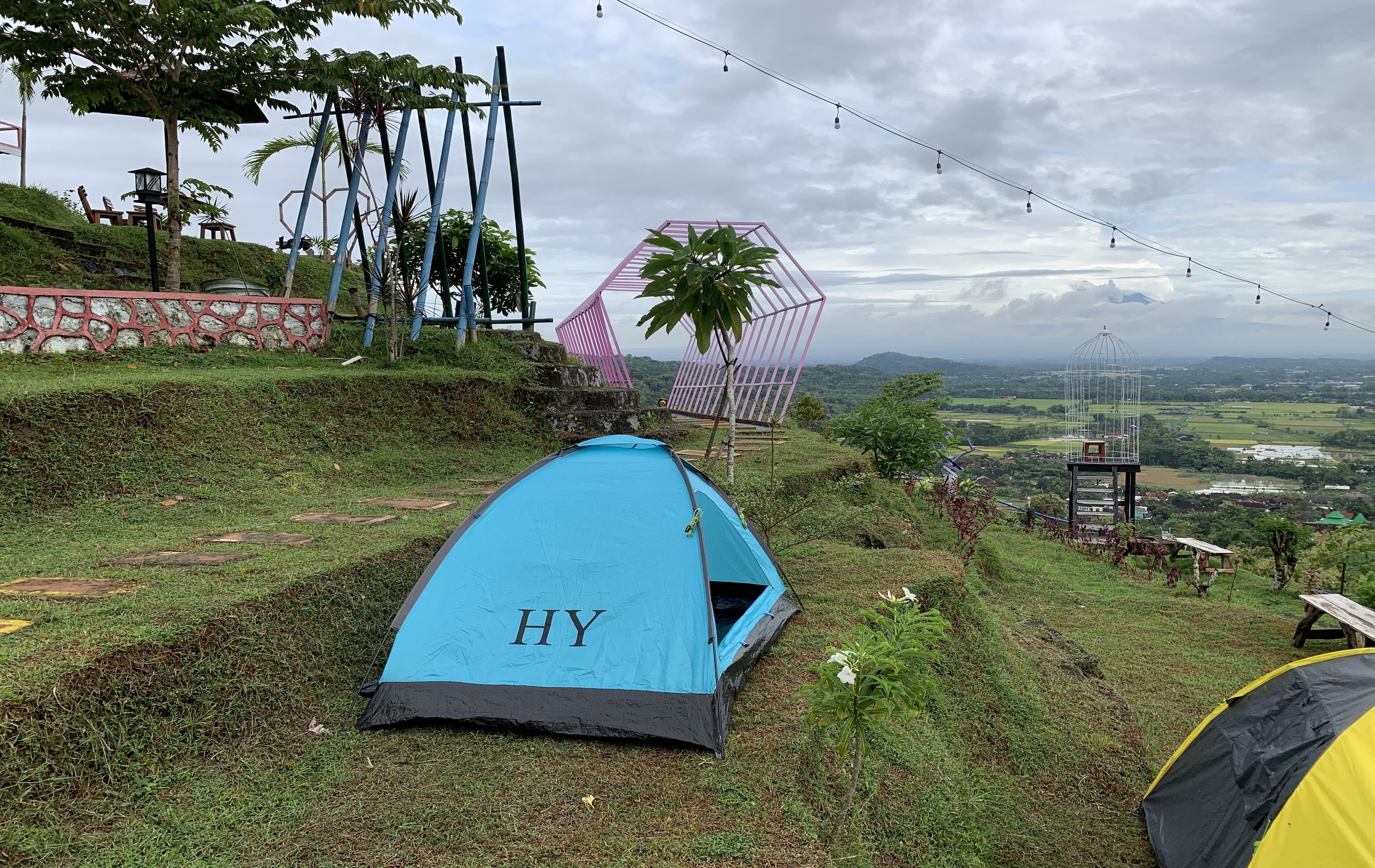 Una tenda blu con l'etichetta 'HY' su una collina erbosa, vista sulla campagna.