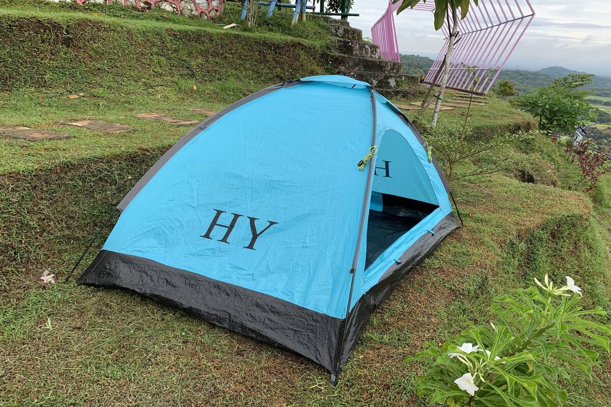 A blue tent with the letters "HY" on its side, set on a grassy hill with a view of the landscape.