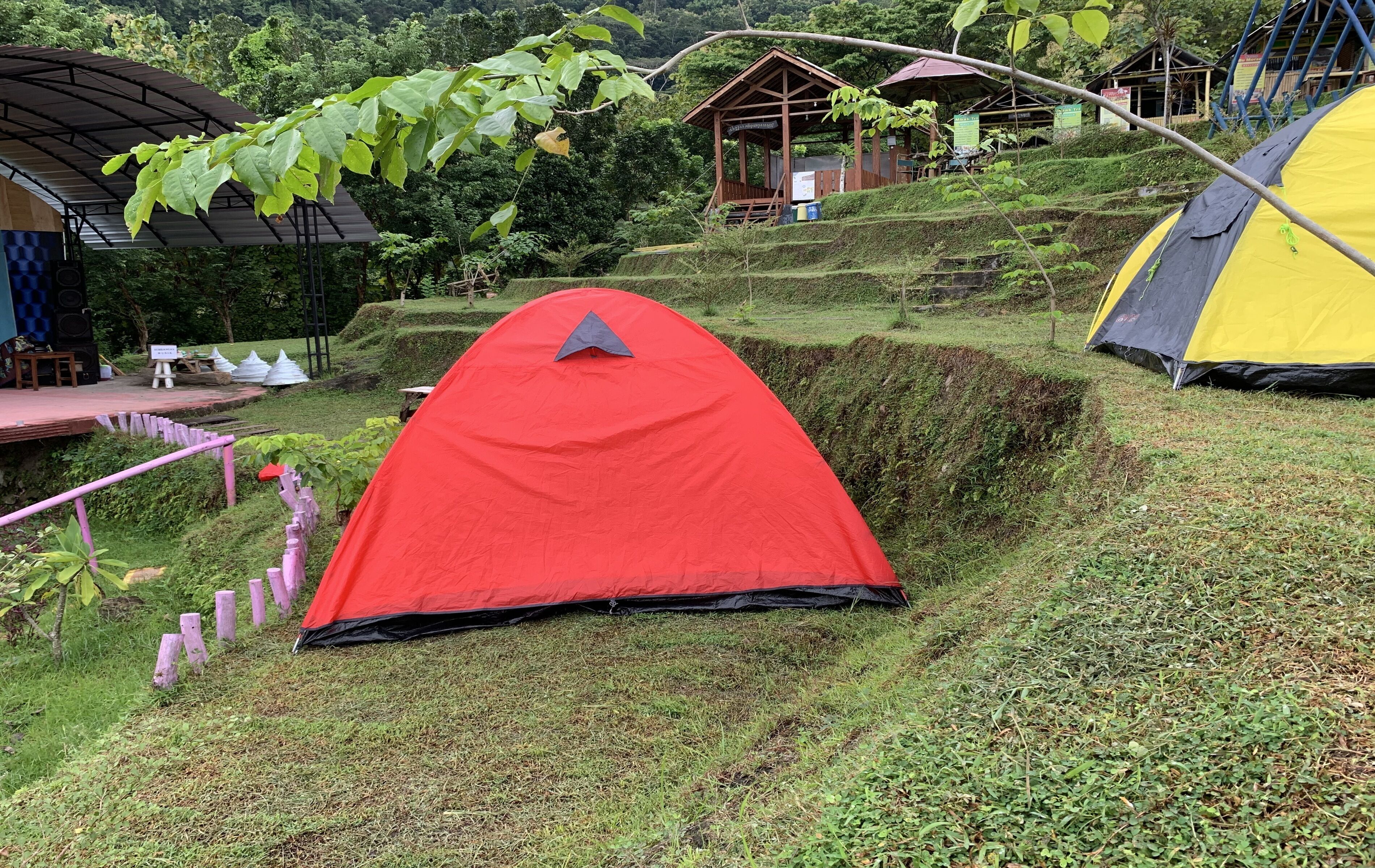 A red tent set up on a grassy slope with terraced fields in the background.