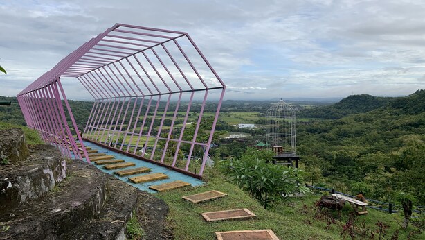 Una estructura metálica rosa con cerramiento de vidrio que da a un valle exuberante.