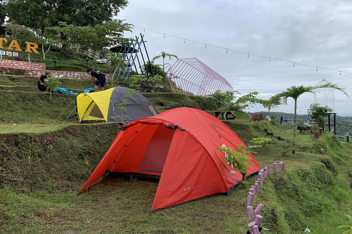 A red tent and a yellow tent set up on a grassy hill with a view of a large structure in the background.