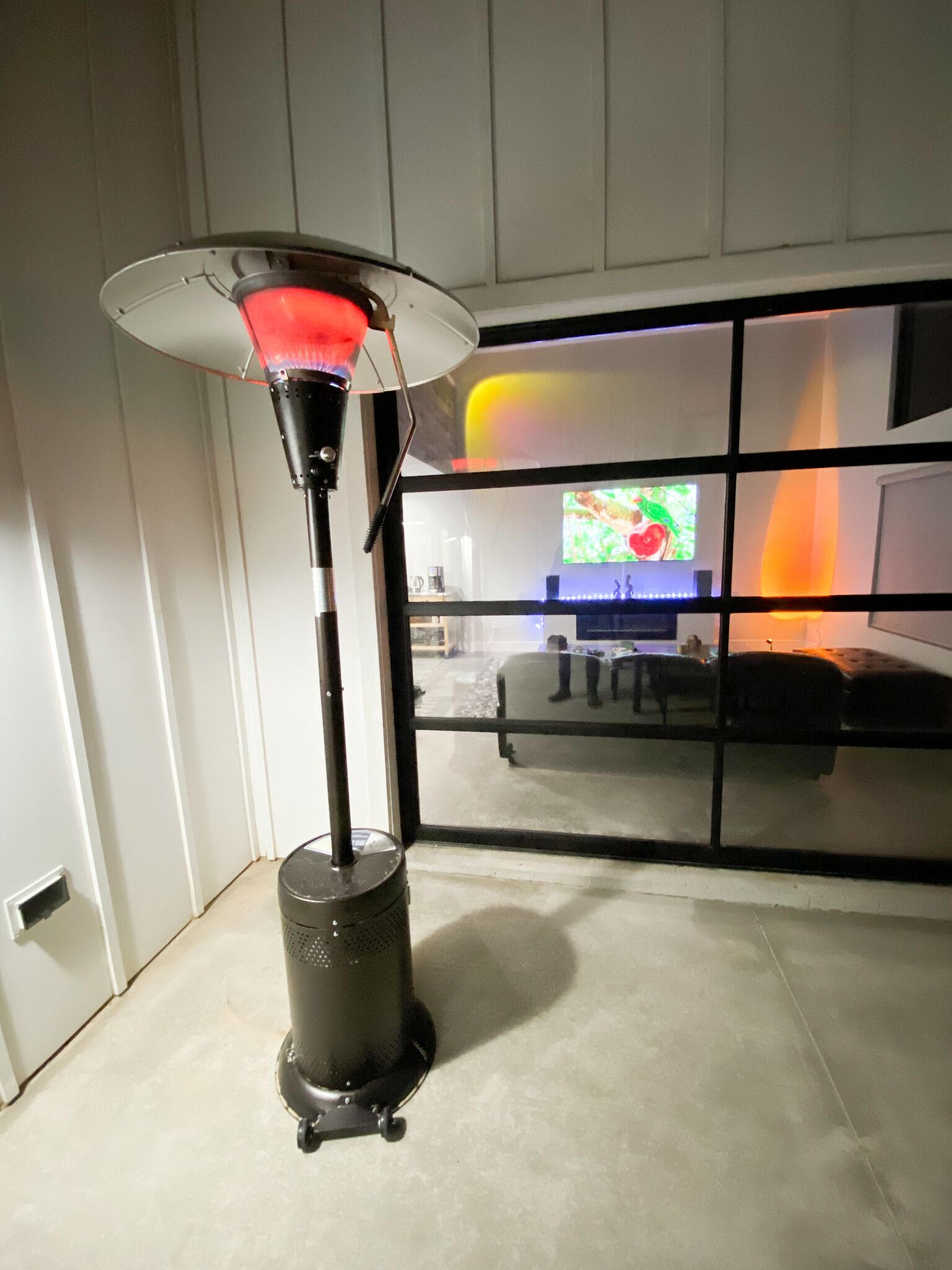 Une pièce avec un radiateur mobile, une fenêtre donnant sur un coin cuisine et une grande fenêtre à carreaux.