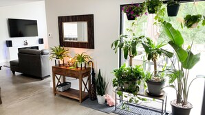 Una sala de estar moderna con un sofá, una mesa de centro de madera con plantas, un espejo grande y un televisor montado en la pared.