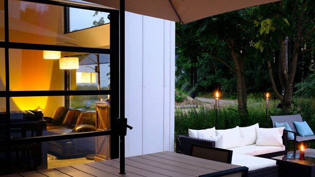 Un patio al aire libre con una mesa y sillas de madera, un sofá con cojines blancos y una mesa de centro de vidrio.