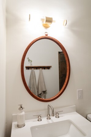 A bathroom with a round mirror, a white sink, a towel rack, and a wall-mounted light fixture. - Cozy and Stylish Vibes in Midtown Tucson Home (Tucson)