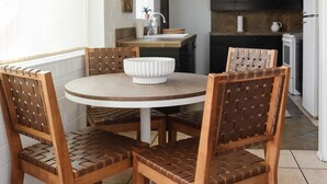 Un coin repas avec une table ronde et quatre chaises en bois dont les dossiers sont en osier tressé. Un bol blanc est posé sur la table.