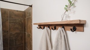 Un porte-serviettes en bois avec deux serviettes suspendues, un vase en verre avec une plante et un espace douche avec des carreaux de couleur marron.