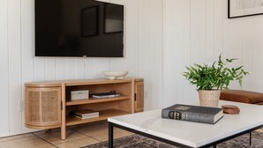 Un salon avec un téléviseur à écran plat fixé au mur, une console en bois sur laquelle sont posés un bol et des livres, une plante en pot et une table basse avec un livre et des sous-verres.