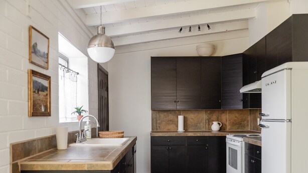Une cuisine moderne avec des meubles de couleur sombre, un réfrigérateur blanc et un plan de travail en bois.