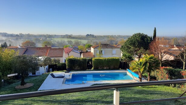 A residential area with a swimming pool, houses with red-tiled roofs, and a view of distant hills.